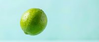 Fresh green lime with water droplets isolated on light blue background, suitable for food and beverage design projects.