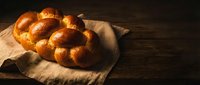 Fresh baked challah bread with golden crust on linen cloth over rustic wooden table. Traditional Jewish braided loaf for Shabbat and holidays bakery concept.