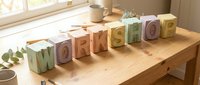 Wooden alphabet blocks spelling WORKSHOP arranged on desk near window with natural lighting and coffee cup for creative workspace design.