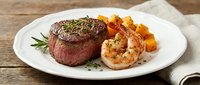 Grilled medium-rare steak with herb crust served alongside roasted shrimp and golden diced potatoes on white plate for fine dining restaurant menus.