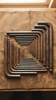 Set of vintage hex keys arranged in geometric pattern on weathered wooden surface creating industrial tool organization display for workshop projects.