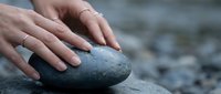 Gentle hands touching smooth river stone in peaceful meditation moment promoting wellness and mindfulness practices for relaxation and stress relief.