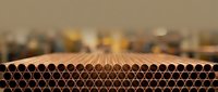 Industrial copper pipes arranged in rows showing circular openings, manufacturing warehouse background with warm lighting for construction projects.
