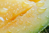 Fresh cantaloupe melon slice with water droplets in extreme macro, showing juicy orange flesh and green rind texture in vibrant colors.