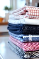 Stack of folded kitchen towels and napkins in red, white, blue, and multicolored patterns, arranged neatly for home organization.