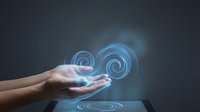 Human hands holding glowing blue spiral energy symbols above digital tablet screen representing technology innovation and futuristic interface design.