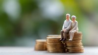 Senior couple figurines sitting on stack of gold coins against blurred green background, representing retirement savings, pension fund and financial security.