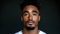 Young African American man with curly hair and facial hair looking confidently at camera against dark green background, studio portrait highlighting natural expression.