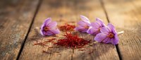 Purple saffron crocus flowers with red stigma threads on rustic wooden background. Aromatic spice ingredient for cooking and culinary applications.
