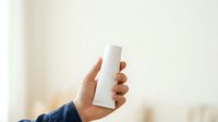 Male hand holding white cylindrical product bottle for skincare, cosmetics, or personal care packaging mockup.