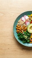 Nutritious Buddha bowl with roasted chickpeas, quinoa, fresh vegetables, kale and radish slices on wooden surface for healthy eating and wellness content.