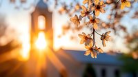 Delicate cherry blossoms backlit by golden sunset rays with church steeple silhouette creating spiritual spring atmosphere and natural lens flare effect.