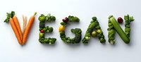 Fresh vegetables arranged to spell VEGAN word with carrots broccoli and leafy greens on white background promoting plant-based lifestyle and healthy eating.