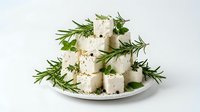 Cubes of fresh white cheese with rosemary sprigs and herbs on white plate, isolated on white background for food styling and culinary design use.