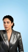 Young woman of Middle Eastern descent wearing charcoal gray blazer against light blue background, suitable for corporate, business, and professional headshot applications.