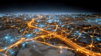 Aerial view of glowing urban network with orange and blue light trails representing digital connectivity and smart city infrastructure.