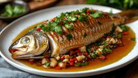 Whole grilled fish with herbs and spices in savory sauce on white plate. Traditional Asian cuisine dish with fresh garnish and colorful vegetables.