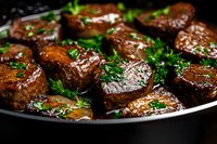 Juicy grilled beef medallions garnished with fresh parsley and herbs on dark plate. Tender meat pieces in savory sauce, close up view of gourmet steak dinner.