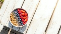 Acai smoothie bowl topped with fresh blueberries, raspberries, granola, and chia seeds on a rustic white wooden table in sunlight.