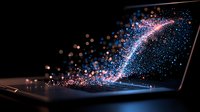 Glowing particles streaming from laptop screen in dark room creating magical light trail effect with blue and pink sparkles against black background.
