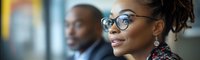 Young African American businesswoman wearing glasses smiles confidently during corporate meeting, displaying professional leadership and success in modern office setting.