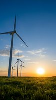 Wind turbines in a row across a green field at sunset, generating renewable energy for sustainable power production and clean electricity generation.