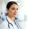 Professional female doctor with stethoscope in white coat smiling confidently in modern medical clinic environment for healthcare marketing materials.