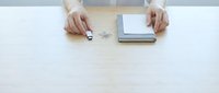 Hands of a young woman on a wooden desk with a USB flash drive, paper clips, and a notebook, top view office workspace concept.