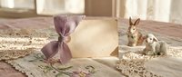 Easter greeting card with purple ribbon bow and decorative bunny figurines on rustic wooden table with natural lighting for spring holiday celebrations.