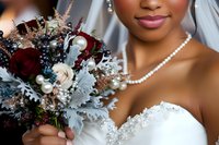 African American bride in white wedding dress holding romantic burgundy and white bouquet with dusty miller leaves, pearl necklace detail, close up portrait on wedding day.