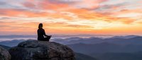 Woman meditating on mountain peak at sunrise with colorful sky and layered hills. Peaceful mindfulness practice in nature for wellness and spiritual growth.