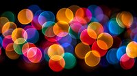 Colorful bokeh lights creating magical atmosphere with vibrant circles of blue, orange, pink, green and purple hues against dark background for festive designs.