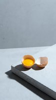 Cracked egg with bright yellow yolk on modern concrete surface with geometric shadows for culinary and cooking concepts.