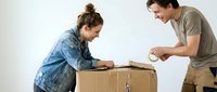 Young Caucasian couple packing cardboard box together during house move or relocation, man and woman preparing belongings for storage or shipping.