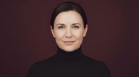 Professional middle-aged Caucasian businesswoman in black turtleneck smiling confidently against burgundy background for corporate presentations.