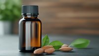 Amber glass bottle with essential oil, fresh green leaves and almonds on dark surface for natural skincare and aromatherapy wellness products.