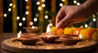 Hand lighting traditional oil lamps during Diwali celebration with warm bokeh lights creating festive atmosphere for Hindu festival of lights decoration.