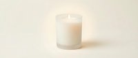 Glowing white candle in a frosted glass jar on a soft cream background, creating a warm, cozy ambiance for home decor and wellness concepts.