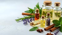 Essential oils in glass bottles with cork stoppers, fresh herbs, lavender, cinnamon sticks and mint leaves on white background for aromatherapy and wellness.