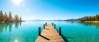 Wooden dock extending into crystal clear turquoise lake surrounded by evergreen forest and mountains under blue sky, suitable for travel and nature backgrounds.