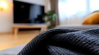 Cozy black knitted blanket on sofa in modern living room interior with TV and natural light from window, creating warm home atmosphere for relaxation.
