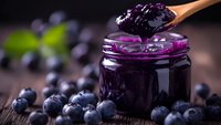 Homemade blueberry jam in glass jar with wooden spoon and fresh berries on rustic table for breakfast and cooking recipes.