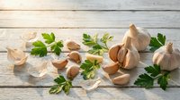 Fresh garlic bulbs and cloves with green parsley leaves scattered on rustic white wooden background for cooking and culinary applications.