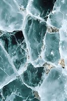 Cracked frozen lake surface with natural turquoise ice patterns and mineral deposits creating abstract winter texture. Suitable for nature and abstract backgrounds.