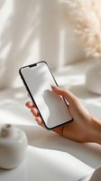 Woman holding smartphone with blank white screen in soft natural light bedroom setting for app mockup and digital design projects.