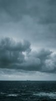 Dramatic storm clouds gather over turbulent ocean waters with a distant cargo ship on the horizon, conveying moody weather and maritime atmosphere for editorial and environmental projects.