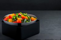 Fresh mixed vegetables diced in colorful cubes including carrots, bell peppers and green beans served in modern black bowl on dark surface for cooking.