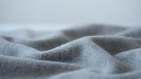 Soft gray fleece fabric with gentle folds and waves creating cozy textile background for comfort and warmth concepts in home decor and fashion design.
