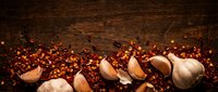 Garlic cloves scattered on rustic wooden surface with red pepper flakes, suitable for culinary, food styling, cooking blogs, and recipe illustrations.