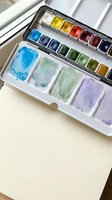 Watercolor paint palette with vibrant pigments and mixed colors on white paper, artistic supplies for creative painting and illustration projects.